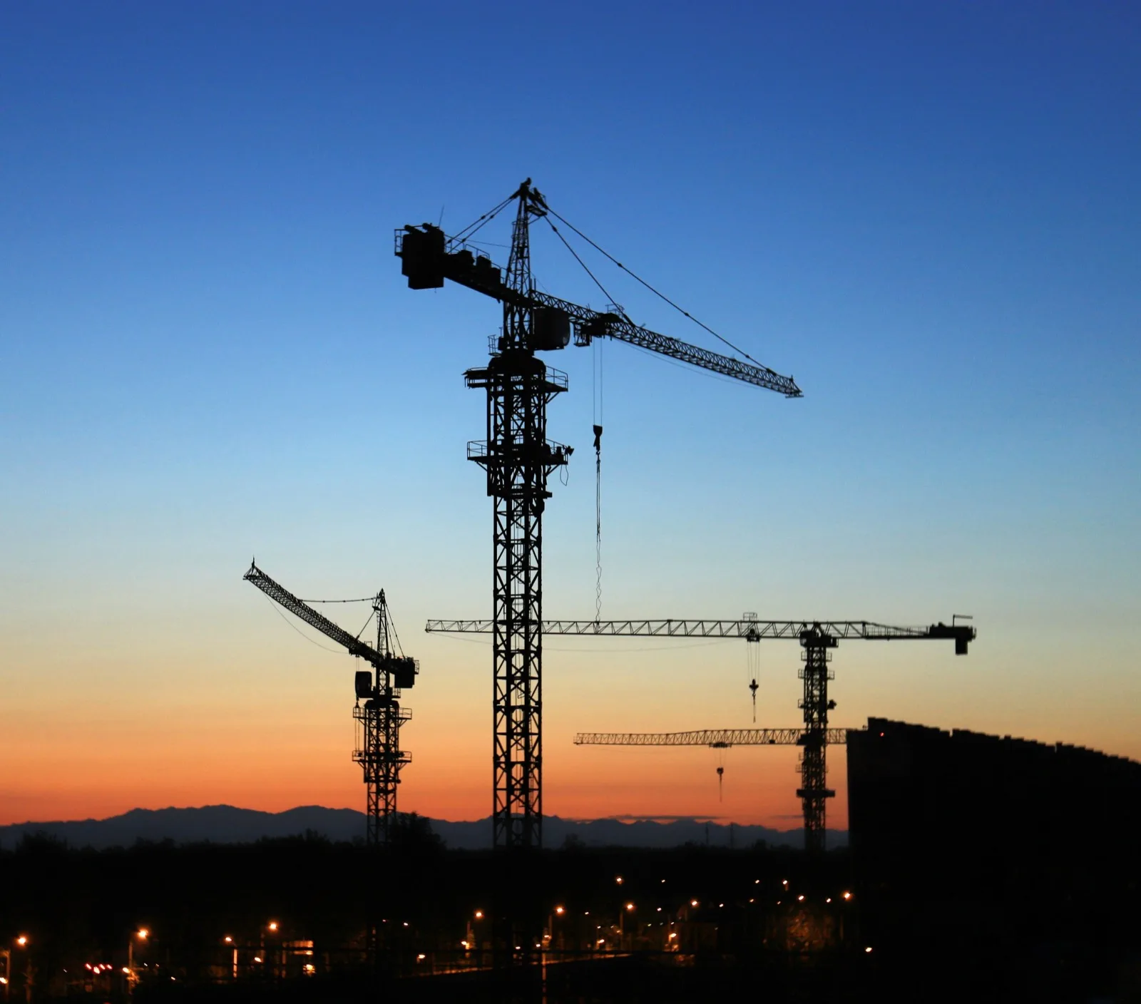 Two tower cranes over a building under construction at golden hour