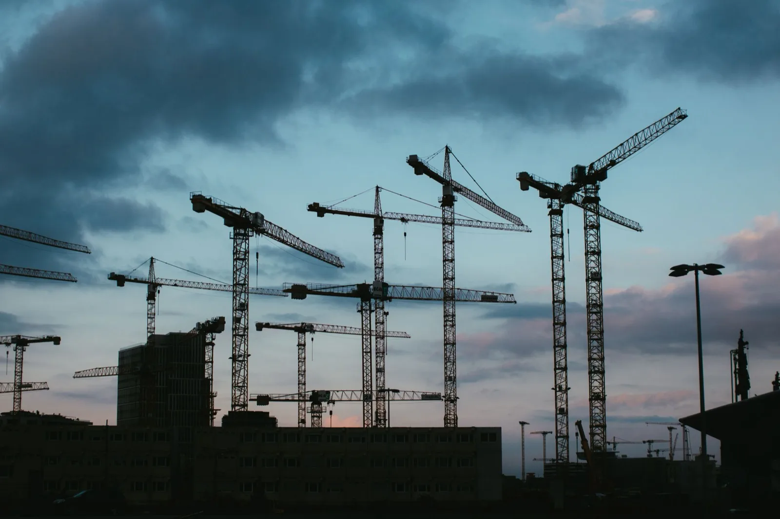 Tower cranes in silhouette under dark clouds at dusk