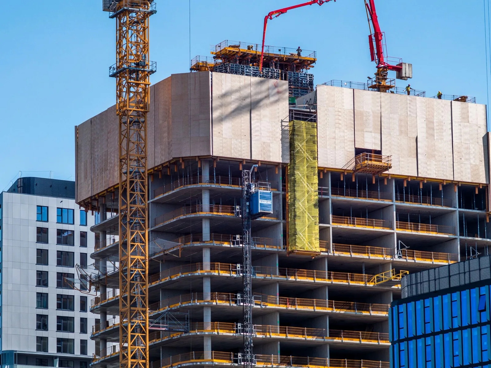 High-rise under construction with a concrete pump and blue enclosure