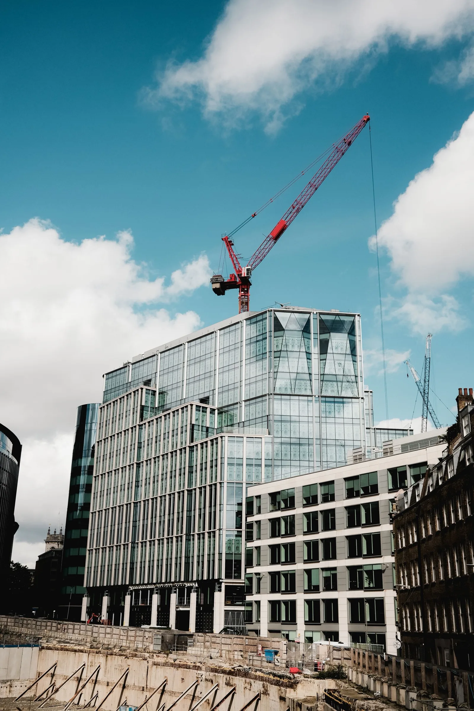 Glass office building under construction with a red tower crane