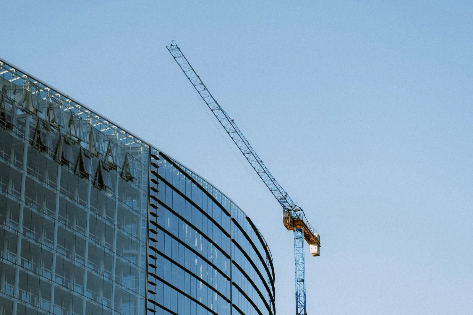 Glass facade under construction with a tower crane against a pale sky