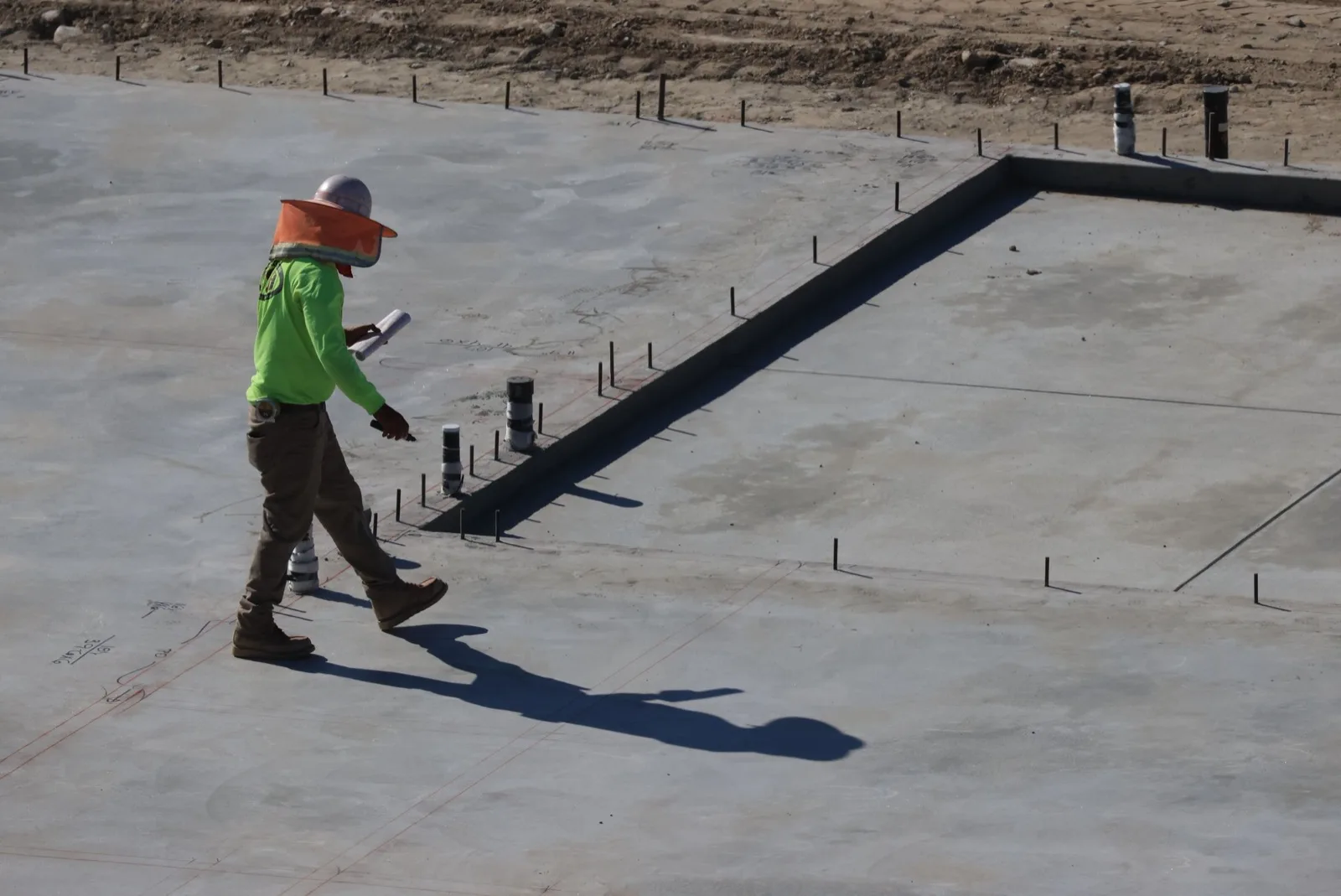Superintendent walking a freshly poured slab with drawings in hand