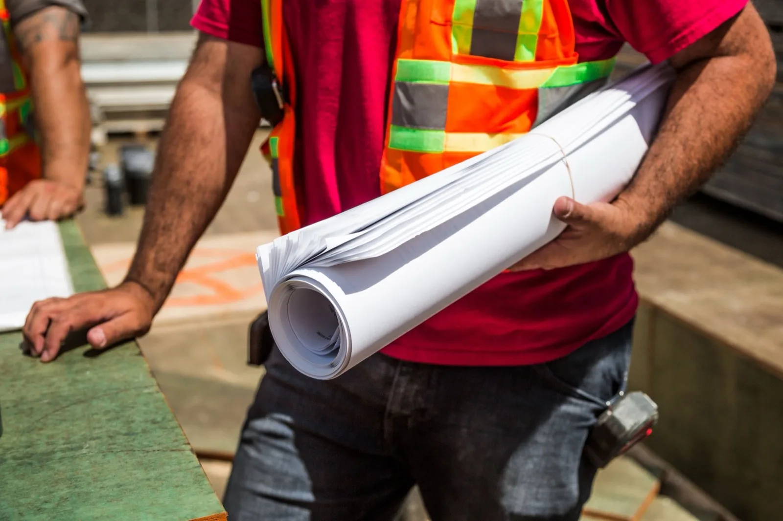 Rolled drawings under the arm of a worker in a safety vest