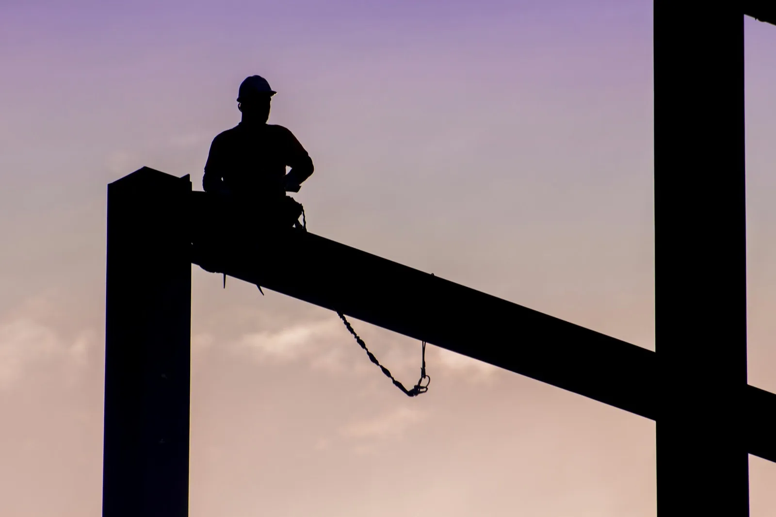 Ironworker seated on a steel column, silhouetted at dusk