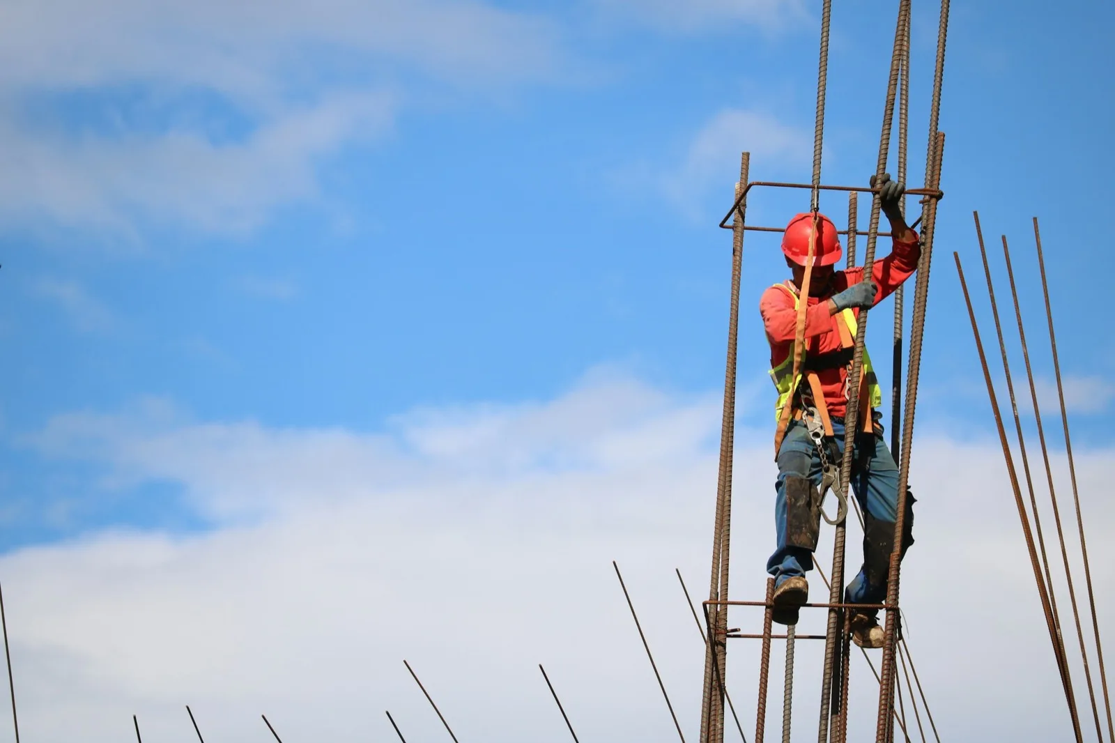 Ironworker on a rebar column against a blue sky with clouds