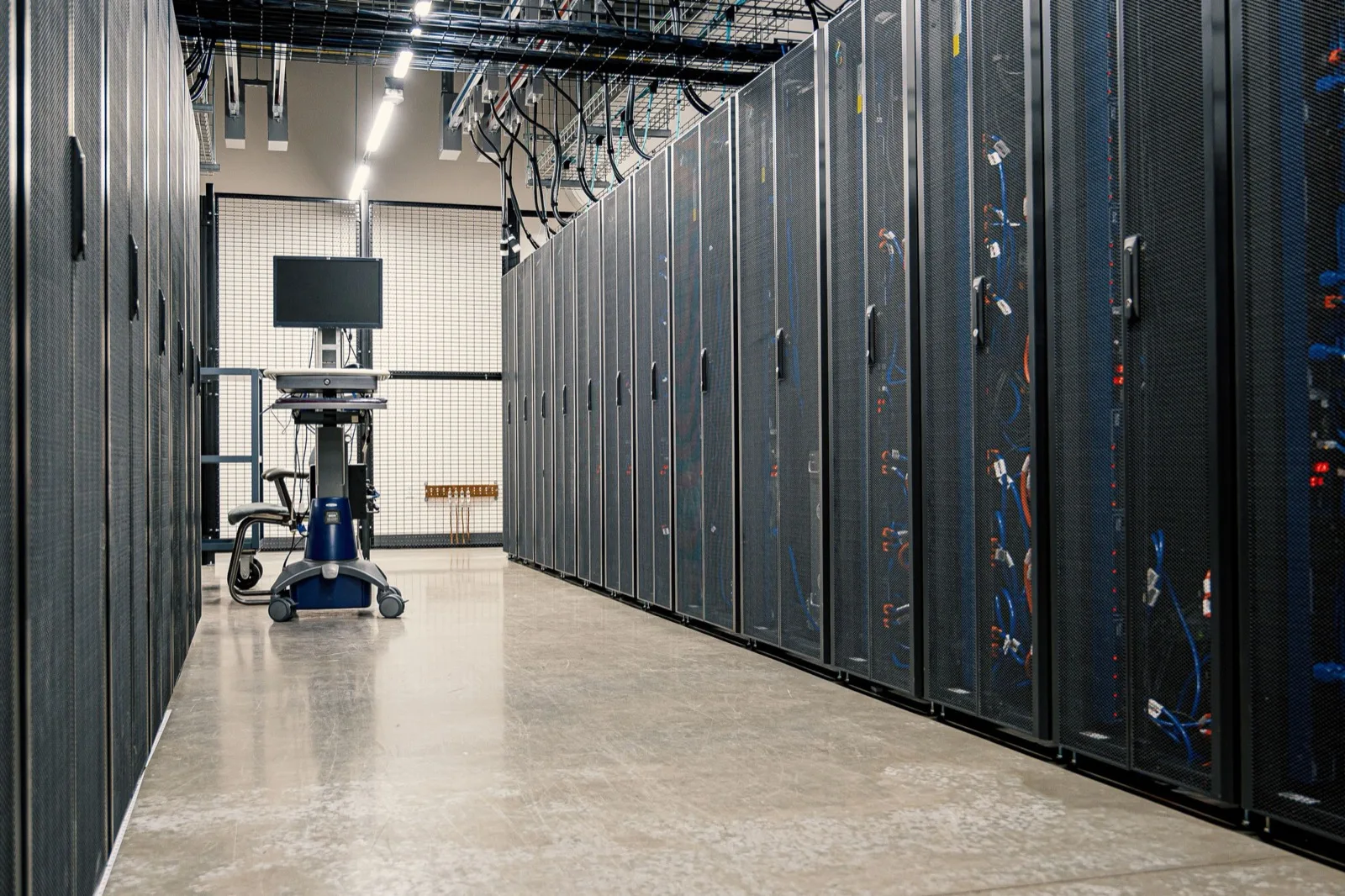 Data hall aisle with a row of black server cabinets and patch cables