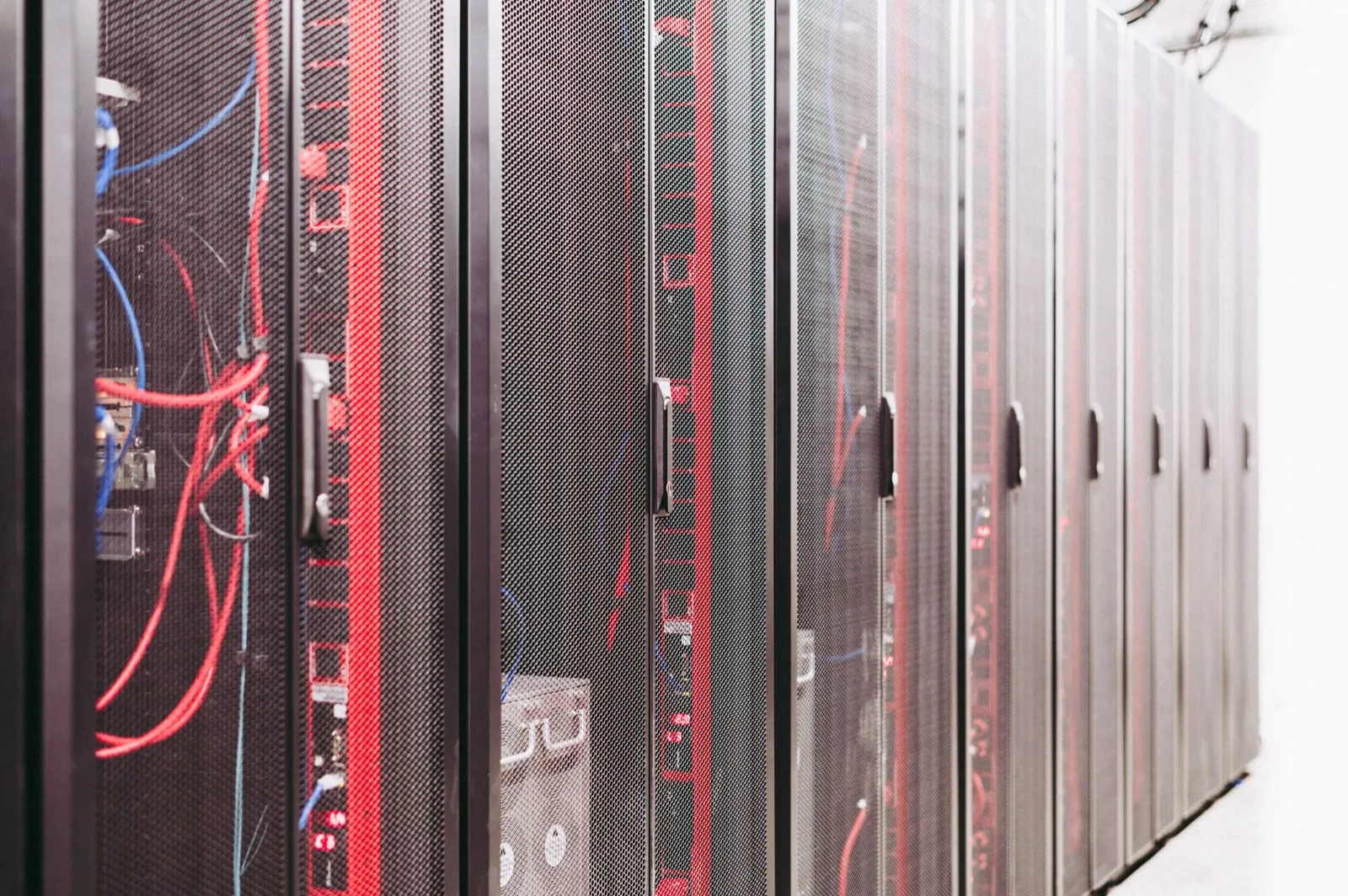 Row of black server cabinets with red patch cables behind perforated doors