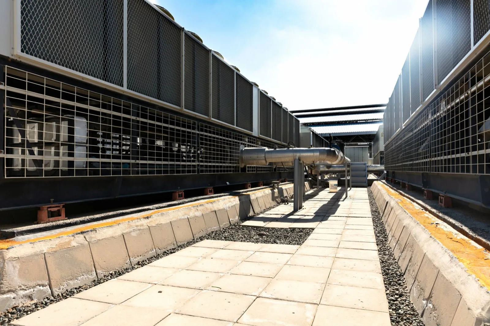 Industrial cooling plant with condensers on both sides of a piped walkway