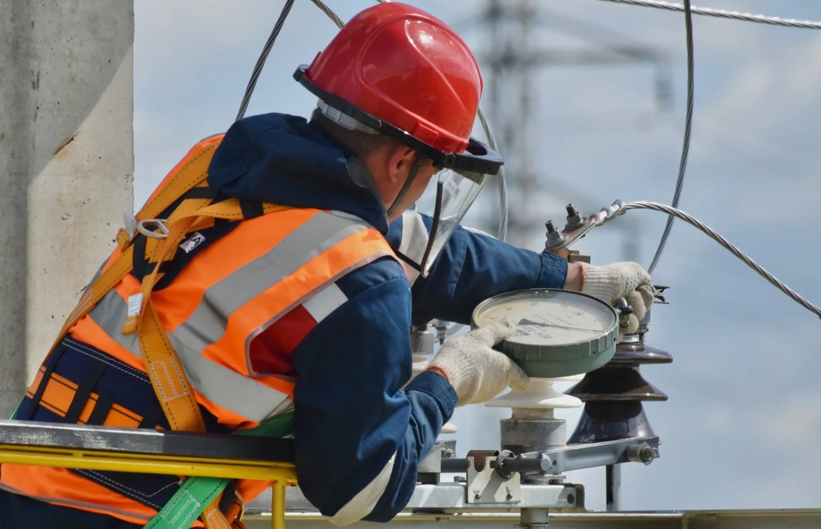 Line worker in a harness and face shield working on a substation insulator